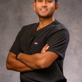 Rohan Shirur poses with his arms crossed, wearing black, medical scrubs